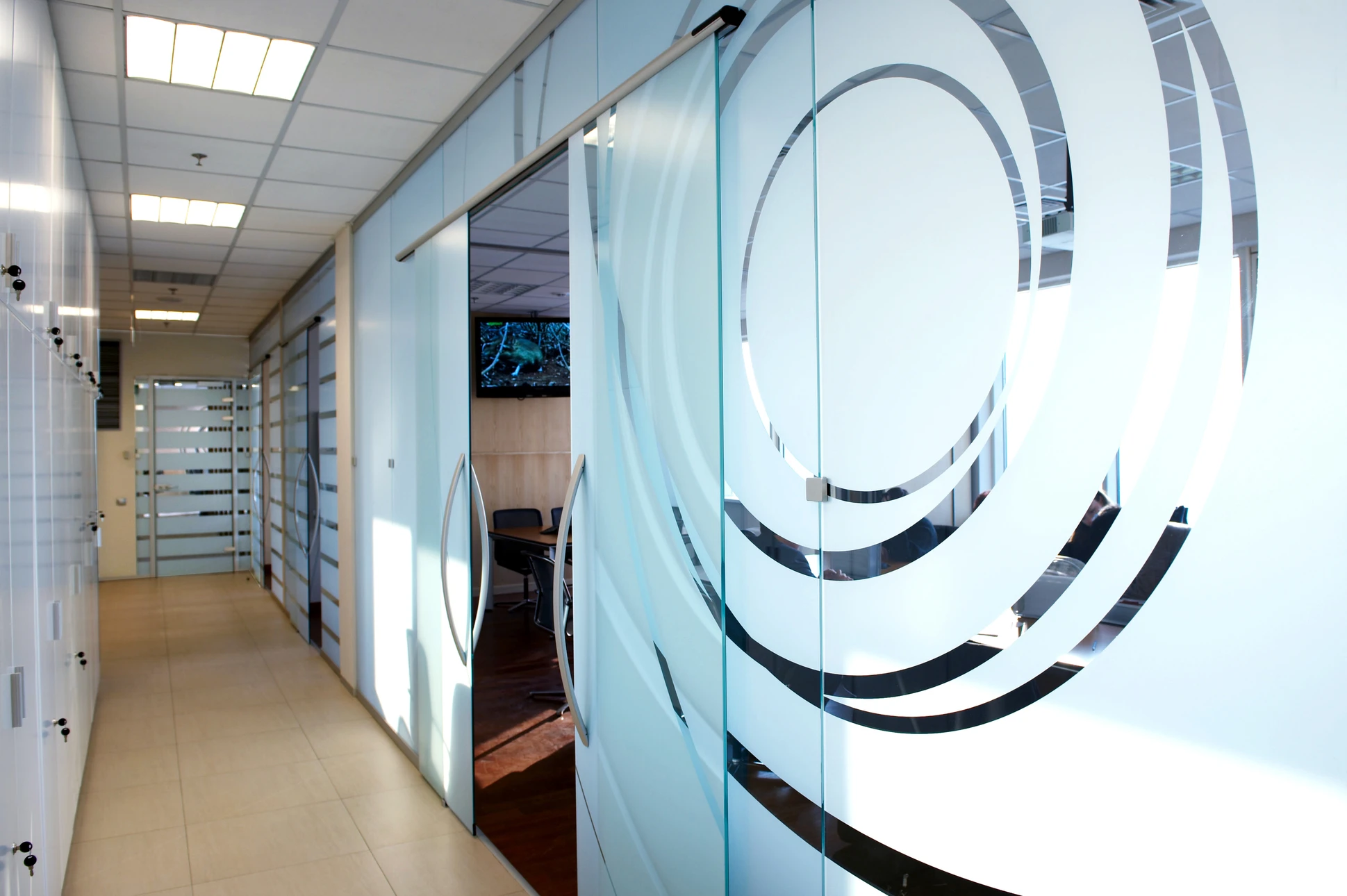 Couloir de bureaux modernes avec cloisons vitrées coulissantes, sol carrelage beige, plafond suspendu avec éclairage LED intégré