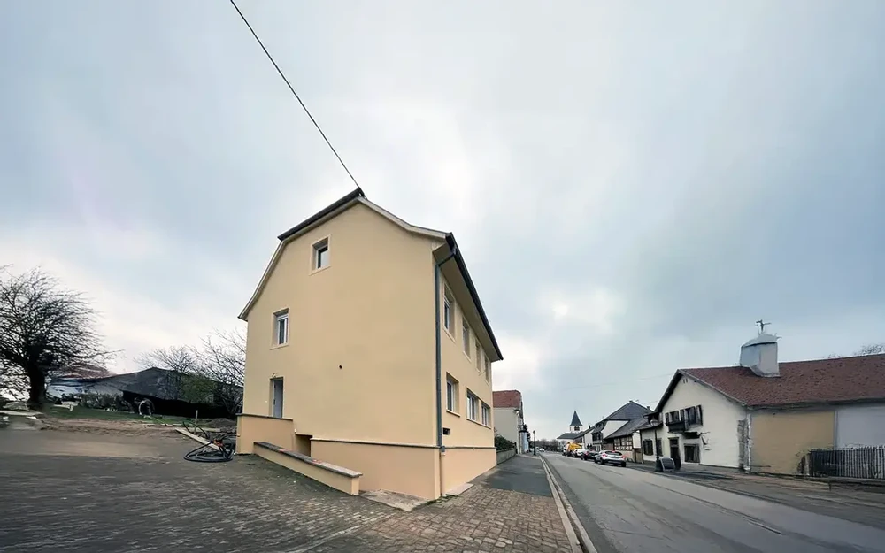 Scène extérieure d'un quartier résidentiel européen avec maisons traditionnelles aux façades colorées, route pavée et ciel nuageux