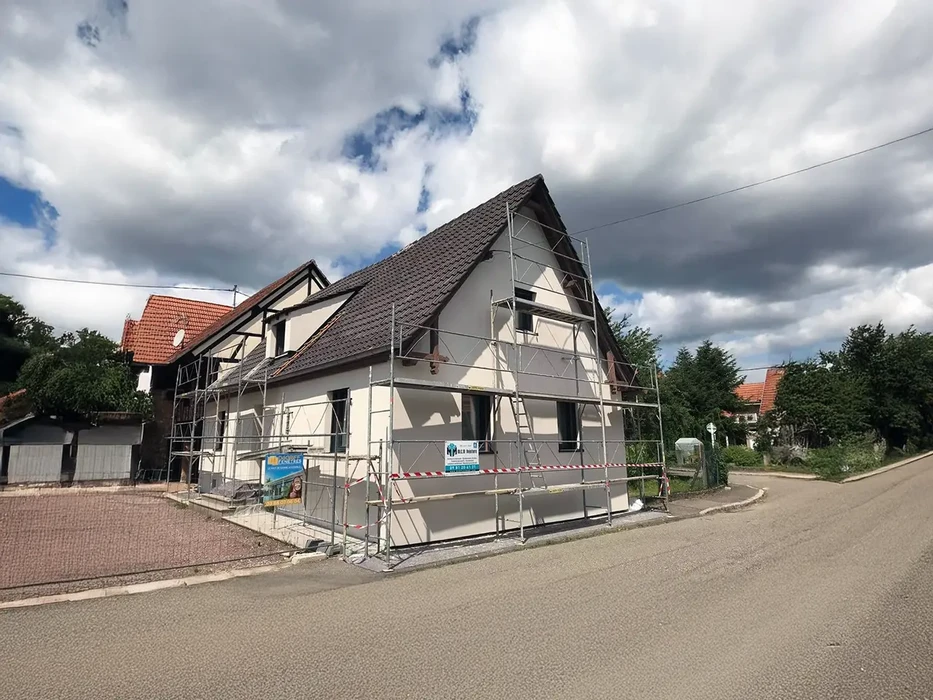 Chantier de rénovation extérieure d'une maison individuelle avec échafaudage métallique tubulaire installé sur façade et pignon