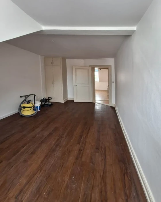 Intérieur d'appartement en cours de rénovation avec parquet en bois foncé fraîchement posé, murs blancs repeints, plafond avec faux-plafond et éclairage LED intégré