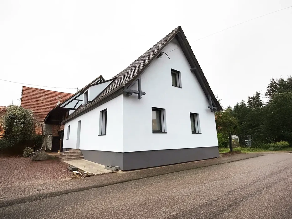 Scène extérieure devant bâtiment résidentiel avec véhicule utilitaire blanc stationné sur gravier