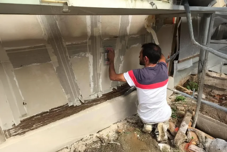 Scène extérieure, main gantée appliquant peinture blanche au rouleau sur mur